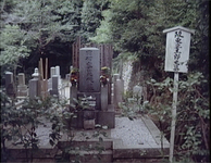 The grave of Bando Tsumasaburo has carved calligraphy on its face. It is marked by a wooden sign with his name to the right of the grave.