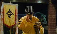 A man bows his head next to a banner with black and red calligraphy.