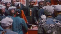 A group of people gather around a red candle. Calligraphy is visible on the wall behind them.