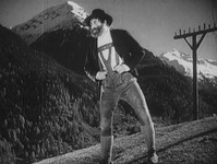 A man stands on a mountain slope. An electricity pole is behind him.