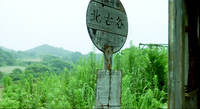 A sign in front of an entranceway has black calligraphy printed on it.