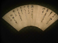 A spread open and lit up fan laying on a patterns background has black calligraphy printed on it.