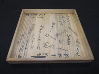 Photograph of a wooden box lid with black calligraphy.