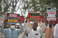 Men walk down a road holding anti-­kidnapping signs. Two of the most prominently displayed signs read “End Banditry Now” and “End Boko Haram.”