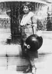 Fig. 64. Hurston stands before a fountain, holding a dark hat in her hand and wearing heeled shoes, looking at the camera.