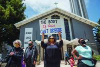 The image shows several members of Columba’s Catholic Church during a Black Lives Matters protest outside their church building. At the center there is female African American holding a sign that reads, “The Body of Christ Can’t Breathe.”