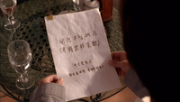 An individual holds a piece of paper with black calligraphy written on it.