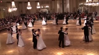 Pairs of formally dressed people dance a waltz. Each couple spins as they step in time to the 1-2-3 pattern in the music.