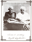 The two collaborators sit at a desk, Anthony looking at a book and Stanton writing on a sheet of paper. Both have white hair and full-length dresses; Anthony wears spectacles.