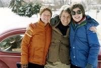 Color photo. Poore, Kaufman, and Cohen stand in the snow, bundled up in warm coats, arms wrapped around each other. All smile toward the viewer. Cohen squints in the bright sun.