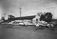 A large pile of Alumnacraft canoes in front of an old wooden warehouse.