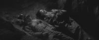 A relatively narrow dirt trench fills the center of the screen at a slant, from top Left to bottom Right. Above and below, only the night-­darkened dirt. His head resting on dead men’s helmets, Mikami lies unconscious, but very straight and composed, even peaceful looking. Harumi, a fantasy in her eye, lies straight and prim beside him, composing an absurd imitation of standard Japanese wedding portrait photography.