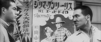 A medium shot that displays a broad poster for a Fox Western from the center frame to Left. In front, on the Left, is an uncertain Kiroku. On the Right, his sneering mentor Turtle cajoles him into a brawl with the other students.