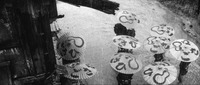 A film still of a rainy and muddy street, with several pedestrians and their calligraphy-covered umbrellas viewed from above.