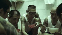 A shot from True Emotion behind the Wall showing inmates eating in a cell, all with tattoos on their body.