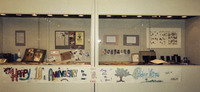 Glass showcases hold cards, newspaper clippings, type, photos, handmade paper, and antique feminist books. “Happy 10th Anniversary” banner below. See Resources for more.