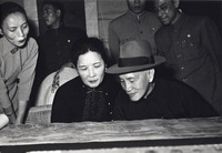 Black and white photograph, Chiang Kai-­shek and Madame Chiang view landscape painting scroll up close, entourage stands behind