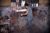 Photograph of John Verissimo from behind, mending a gill net while smoking a cigarette.