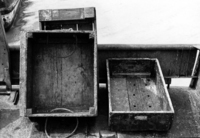 A photograph of three wooden crates, two propped up against a small barrier.