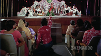 View from audience perspective of Akbar (Rishi Kapoor) and his qawwali party onstage, singing “Parda Hai Parda” in Amar Akbar Anthony. At the top of the frame are the singers, gesturing at the audience. At the bottom and in the foreground are three rows of audience members facing the stage, with Anthony (Amitabh Bachchan) in the center aisle gesturing up at the stage.