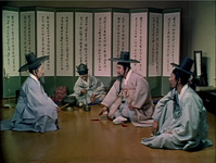 A group of men talk before a typical calligraphic screen.