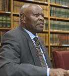 Photograph of Fikile Bam seated in front of bookshelves.