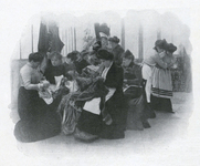 Black-and-white photograph of eight women in long skirts working at hand-sewing in a well-lit room.