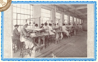 Inside a factory, women add glaze to ceramic spark plugs. Two to four women per work bench sit on tall stools in long row, some with head covers. Two look toward the viewer.