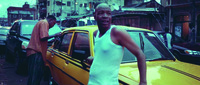 Film still frame of one man leaning on a yellow taxi as another man cleans it