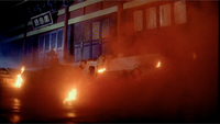 Flames on the floor of a corridor burn in front of a sign on the wall with white calligraphy.