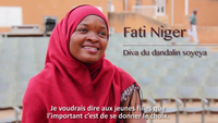 A woman wearing a red hijab smiles at the camera as she sits for an interview. Her name, Fati Niger, is displayed on screen along with subtitles for the interview, which are written in French.