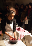 A woman wearing a white apron immerses her hands in a bowl of beets.