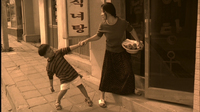 A woman drags a child by the hand next to a door and shop sign with white and black calligraphy in a sepia tint.