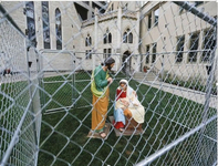 Image of statues depicting Joseph (standing) and Mary (seated) holding baby Jesus, all surrounded by wire fencing outside a church.