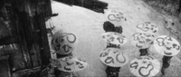 A series of umbrellas have black calligraphy printed on them, in black and white cinematography.