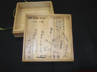 Photograph of a wooden box lid with black calligraphy.