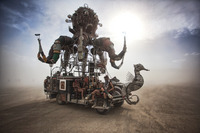 Photograph of Duane Flatmo’s El Pulpo Mecanico, a 12-­foot brass octopus with mobile limbs mounted on a stripped-­down van base, with a six-­foot tall brass seahorse mounted in front like the prow of a ship. The bed of the van, which is open-­air, holds four people clothed in shorts, brass and leather welding goggles, and lace-­up combat boots.