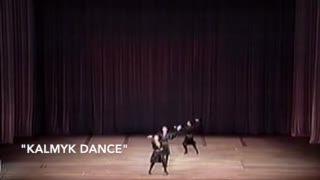 Three men in black folkloric costumes dance on a large stage.