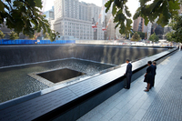 President Obama with his head bowed touches a name inscribed in bronze on the edge of a pool.
