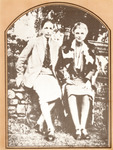 Photo shows the two sitting on a stone wall dressed in skirts and jackets. Hall wears a tie. Hall’s arm is slipped under her partner’s arm, touching Troubridge’s hand.