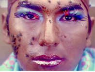 A still photograph shows Bartolina Xixa taken from the end of the video. “Bartolina Xixa: La colonialidad permanente.” It is a close-­up of Xixa’s made-­up face, now covered with flies. Xixa still stares at the camera, bloodshot eyes, in defiance of extinction.} {~?~IM: insert Fig12_01_Robles-­Moreno.jpg here. ALT: Two persons look at the camera, gesturing with open mouths. They wear lipstick, glittery eyeshadow, big eyelashes, wigs, and long earrings.