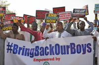 A group of men are pictured marching and chanting as they hold a banner that reads “#BringBackOurBoys.” Many of the men behind the banner hold up anti-­kidnapping signs.