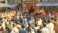 A crowd gathers in the street. Calligraphy is visible on the walls in the background.