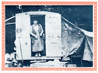 Carr stands at the door of her trailer, smiling; she wears a long dress of printed fabric and a vest. The trailer has a tent-like area on the right; a broom hangs to the left.