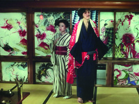 Tight Long Shot of a smug Matsuzaki, off-­center Right, his figure stretching from bottom top, save for a ceiling beam above. Behind his back, turned 45° away from him, is a miffed Madame Mio in kimono. A small writing table is in the botton Left corner. Background is once again the room’s large shōji consisting of obscene paintings. On the top Right, an Edo man horribly stabs a pregnant woman in the neck, her belly also bloodily ripped. Top Left side, a hag-­like ghost stabs a recumbent man. A female corpse is stretched across the bottom panels, with a open space in the middle; bottom corner, the face of a male corpse.