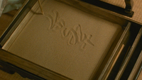 The protagonist writes with a stick on sand.