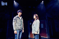 Figure 7.2. In dark lighting, a man and woman face each other, dressed in jackets and blue jeans. Arms hanging down at their sides and legs together, their poses show restraint.