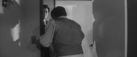 In the center, Hanada, seen from behind in Medium Shot, warily backs away into the open apartment doorway that he just rushed out of a moment before. Right of center, we view the right half of the impeccably-­suited Number One as he also enters the doorway after Hanada, his gun placed directly on Hanada’s (unseen) forehead. Left of screen, on the off-­white, plain wall is the dynamic silhouette of the endangered Hanada. To the Right of Hanada, the open white door and then, across a small, unseen alcove, a wall containing the far larger, more exaggerated shadow of Number One.