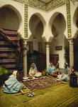 Image of the interior of a house, where a group of women sits in a circle on the floor making a carpet.