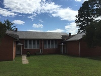 Photo of brick building with side-gable roof and two projecting wings. Doors flank two sets of four, grouped nine-over-nine windows.